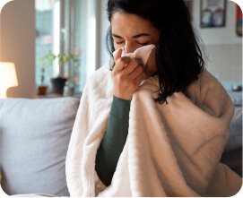 Woman wrapped in a blanket sneezing into a tissue due to cold or fever.